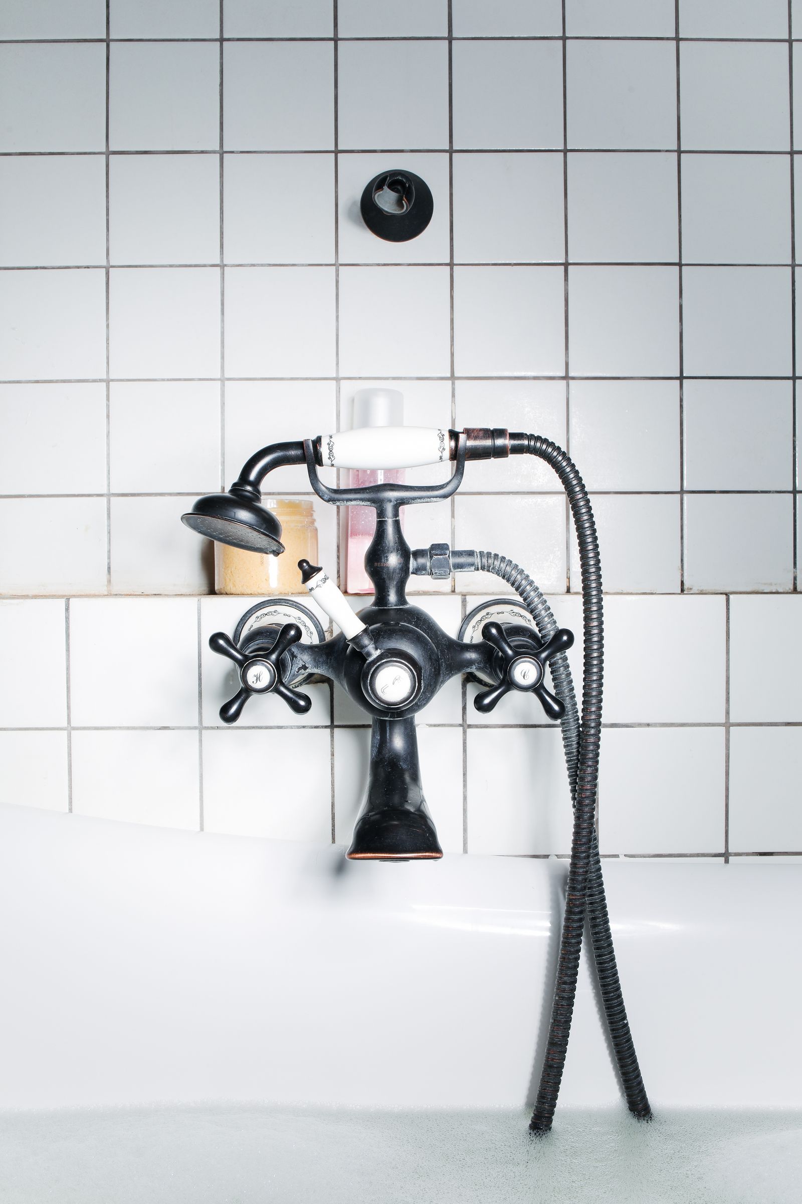 Black freestanding tub faucet against white tile